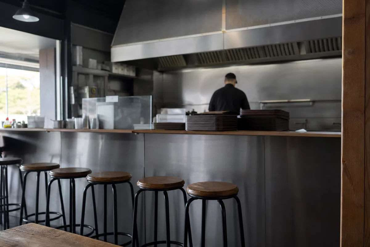 Comptoir de fast-food vu de dos, cuisine ouverte en arrière-plan à l’heure creuse